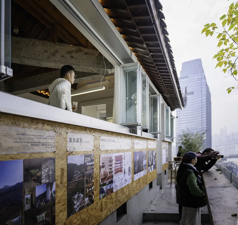 Upper terrace showing exhibition panels on plywood backing beneath a traditional eave with visitors photographing the cityscape
