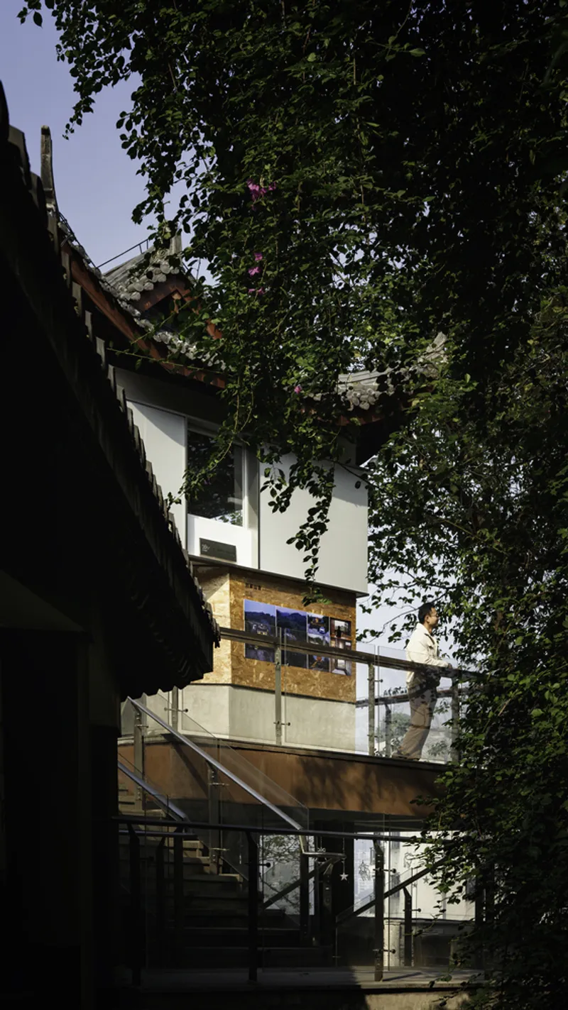 Ground-level view of the glazed entrance beneath the curved tile roof eaves and leafy branches