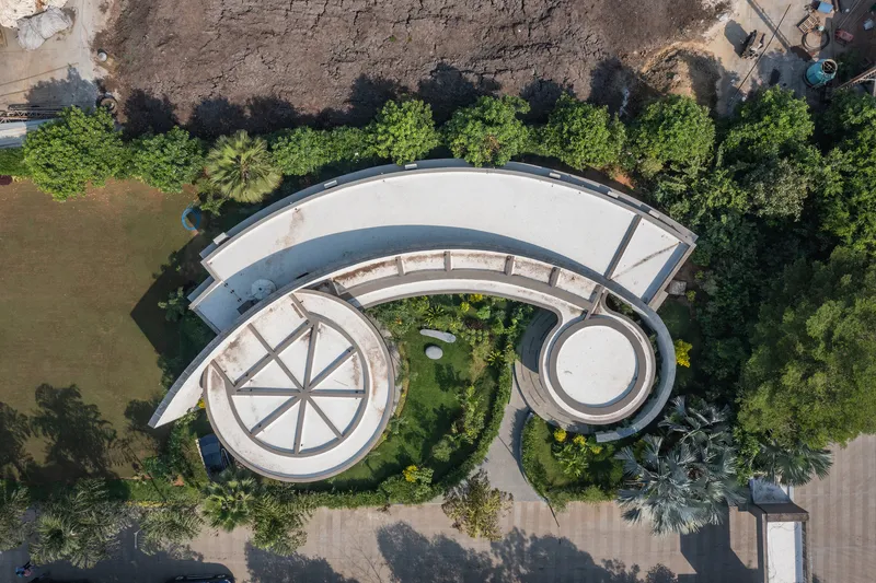 Drone view of the curved roof with circular skylights and landscaped courtyard flanked by trees and bare ground