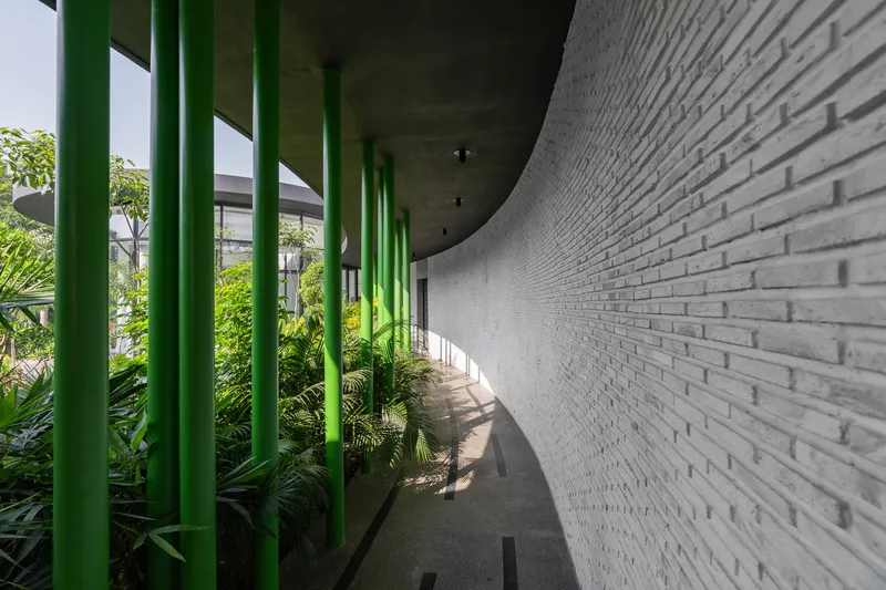 Covered walkway with green steel columns alongside a white brick wall and planted garden beds