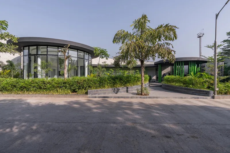 Street view of curved glazed pavilions with planted green roofs and young palms in foreground