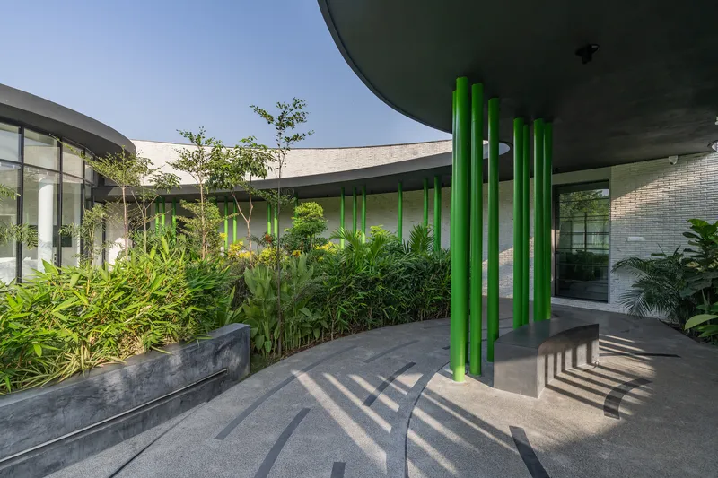Green tubular columns casting striped shadows on the terrace floor beside the planted courtyard