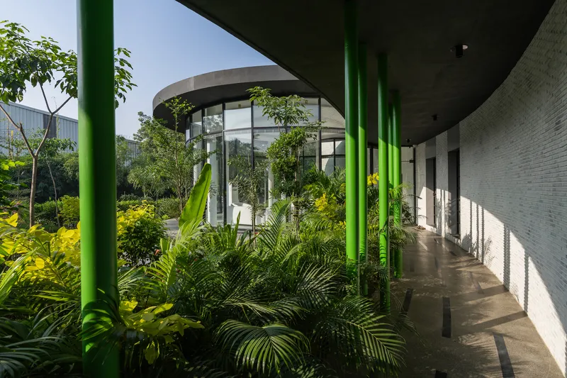 Curved corridor with green columns framing views of the planted courtyard and glazed living spaces