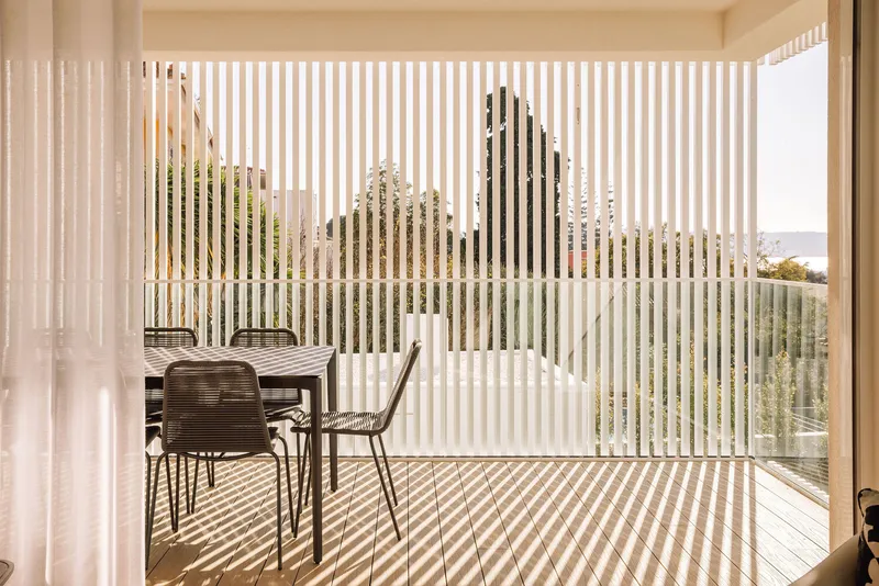 Terrace with vertical screening slats casting striped shadows across the timber deck and dining table