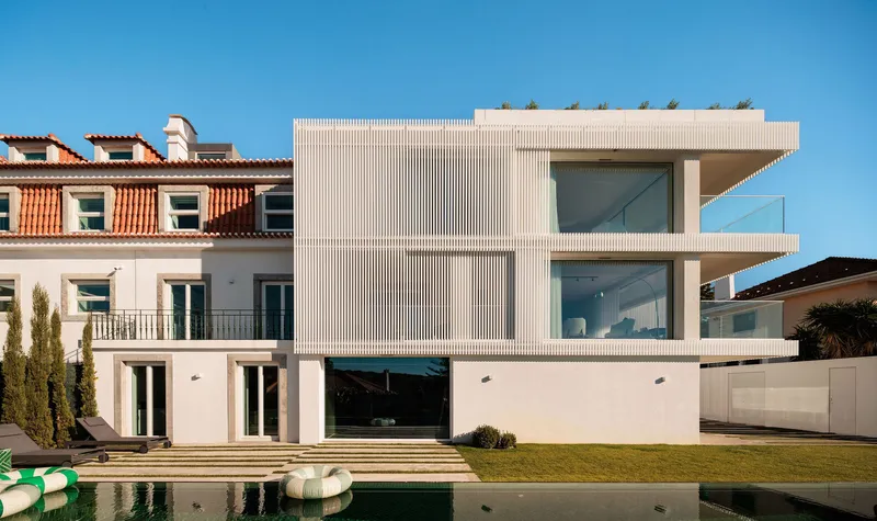 Garden facade with vertical ribbed cladding overlooking the pool and lawn under clear skies