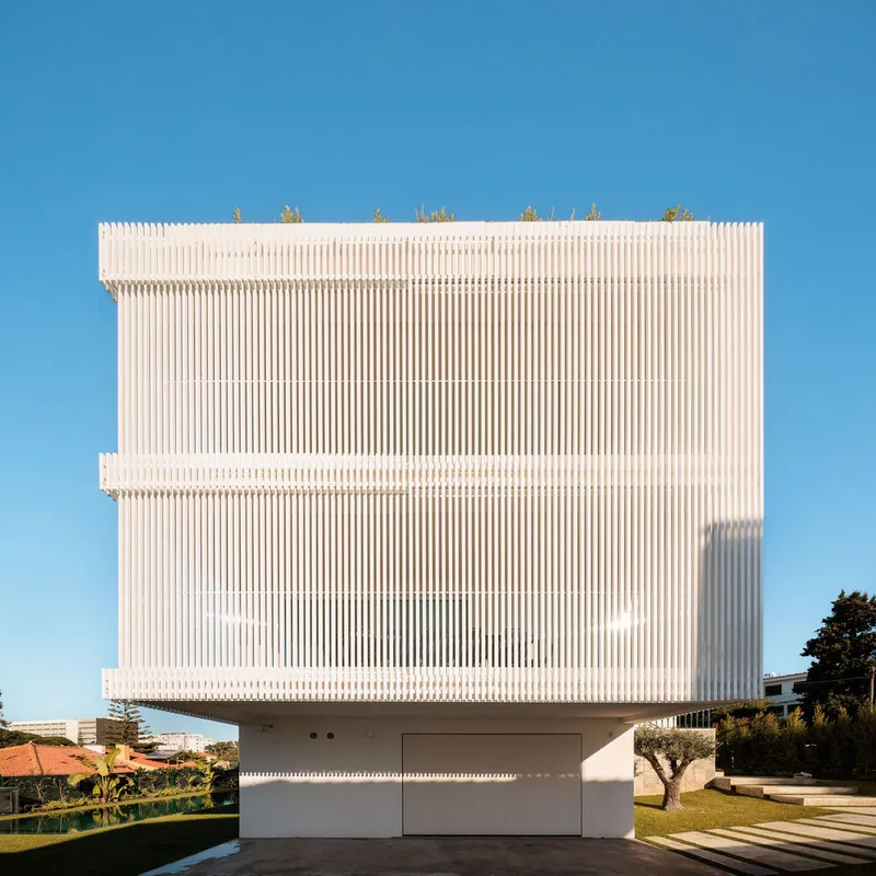 Front elevation of white vertical slat screen wrapping cantilevered upper floors above recessed garage in clear daylight