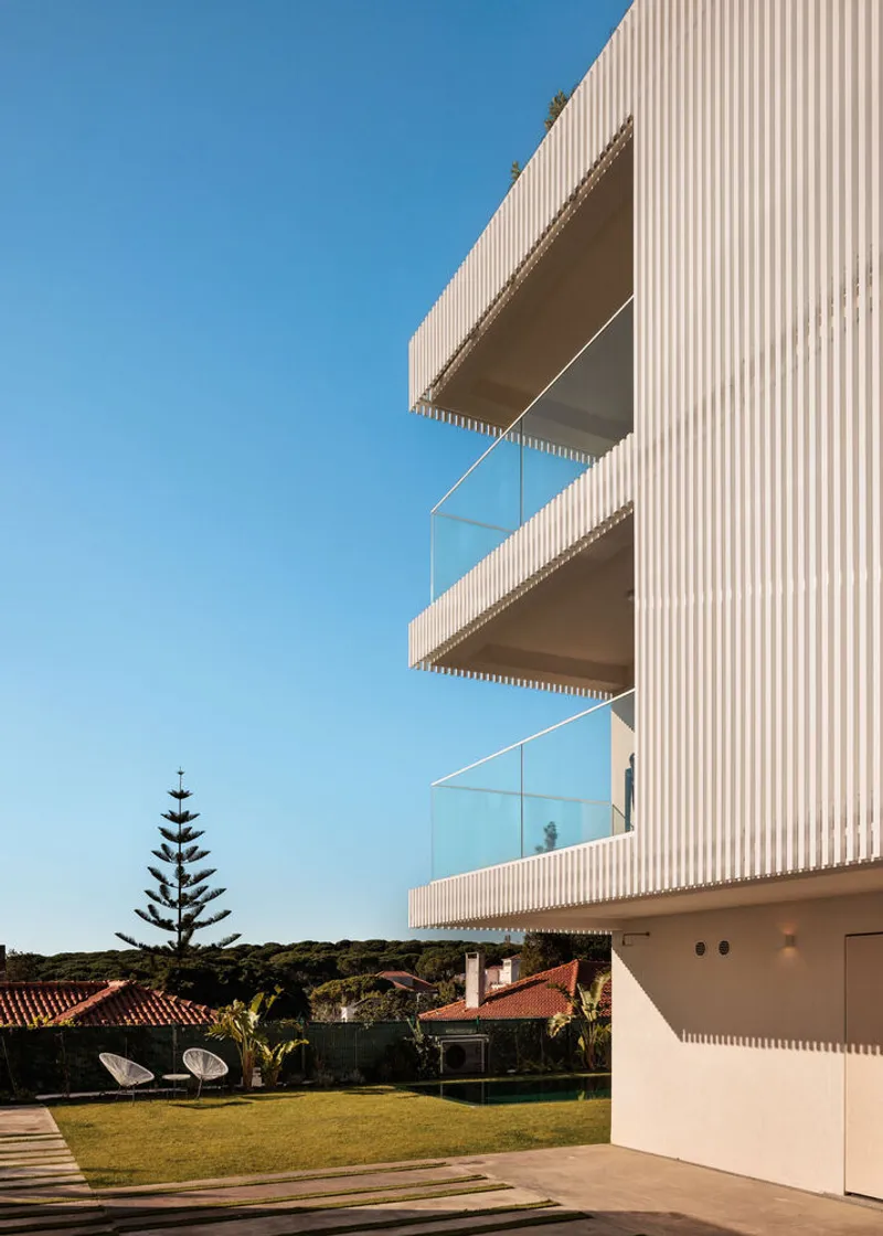 Detail of cantilevered balconies with glass balustrades projecting from facade clad in vertical white slats