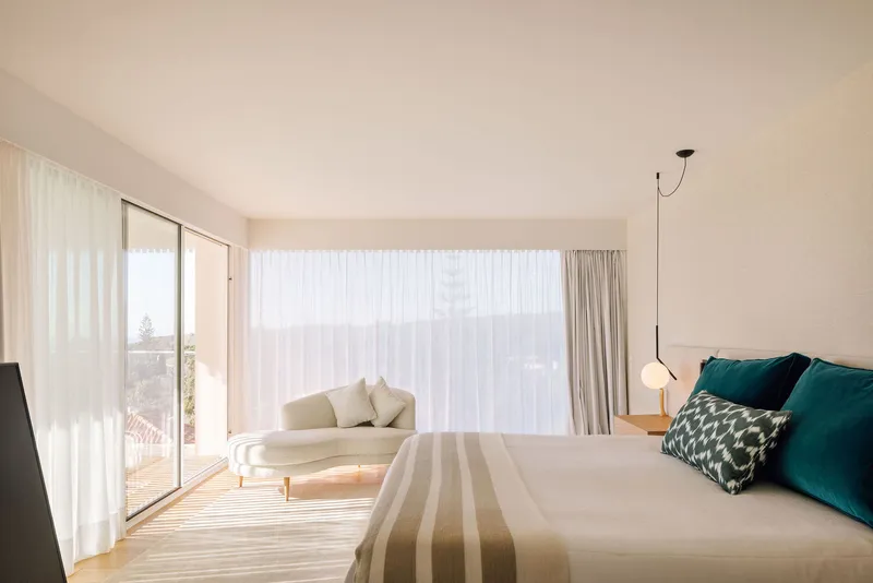 Bedroom interior with daybed seating nook and floor-to-ceiling windows diffused by sheer drapes