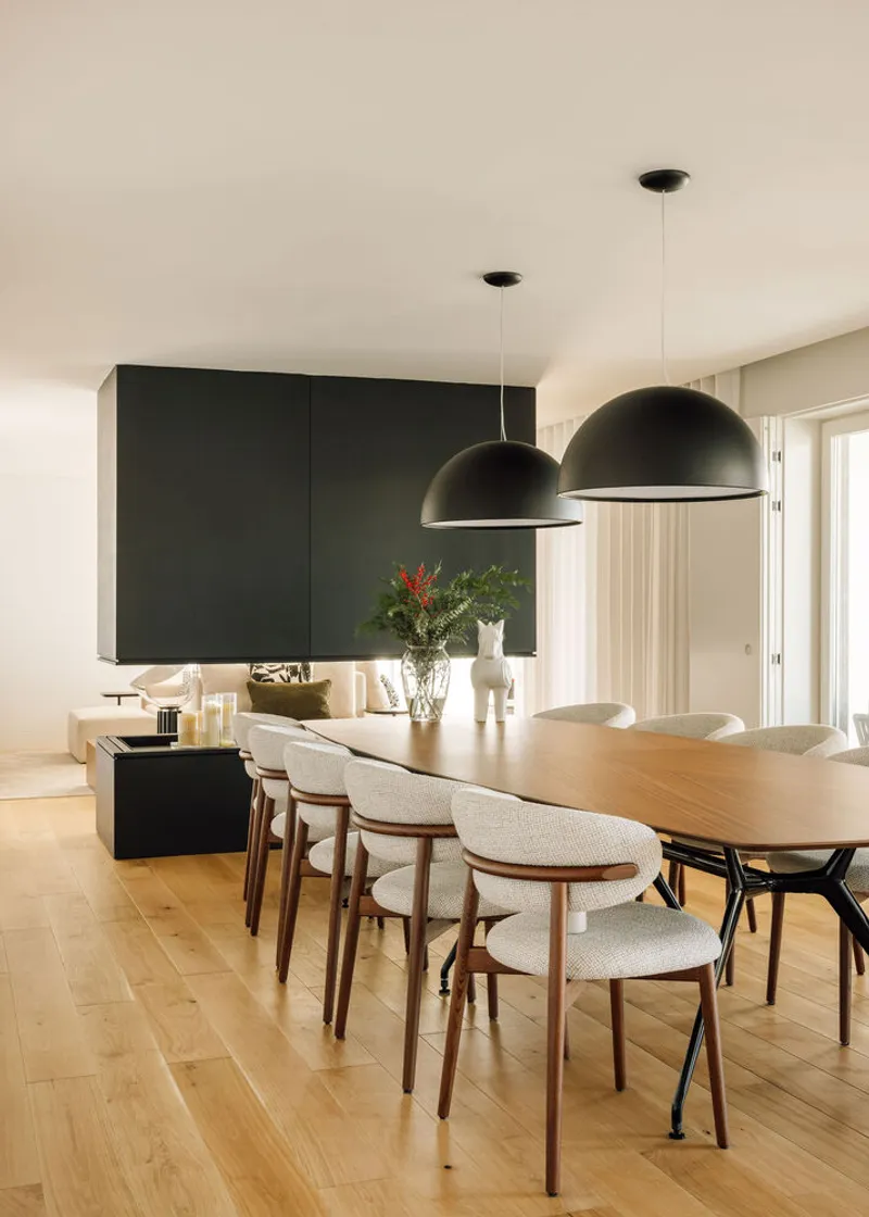 Dining area with timber table and pendant lights beneath a dark kitchen volume