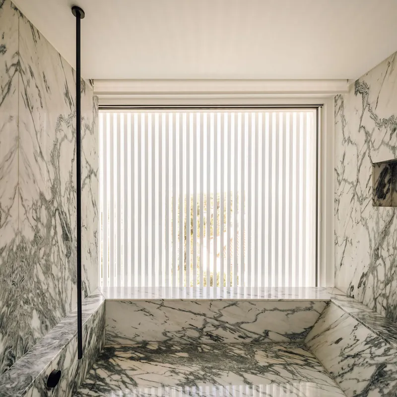 Marble-clad bathtub niche with vertical blinds diffusing daylight through the window