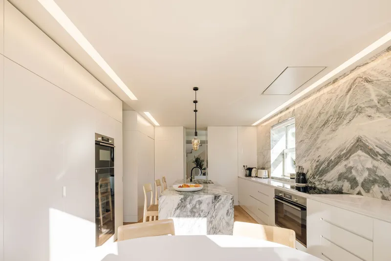 Kitchen with marble backsplash and waterfall island under recessed ceiling lighting