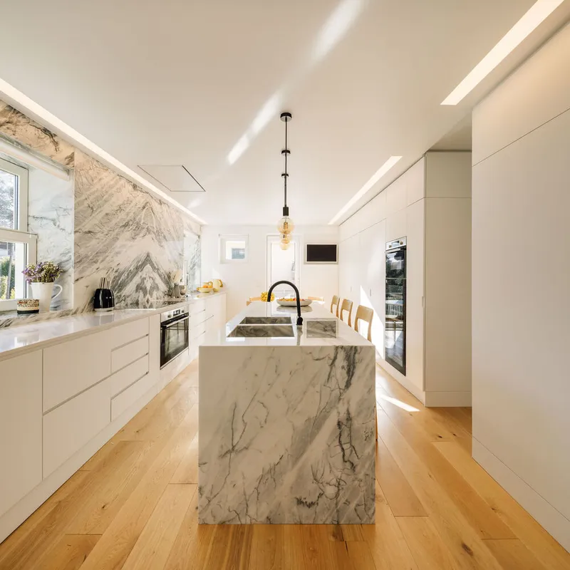 Marble waterfall island with integrated sink beneath a linear pendant fixture