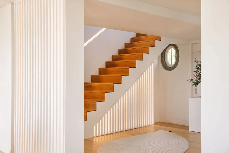 Cantilevered timber staircase with vertical slat balustrade beneath a plywood ceiling and oval window