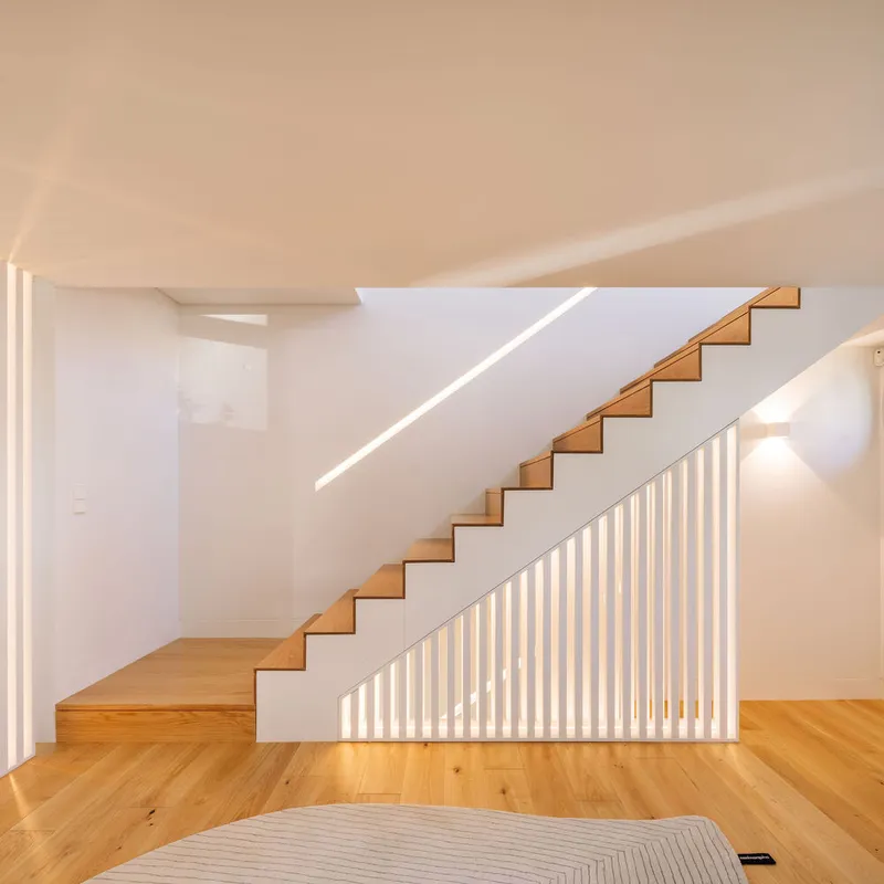 Timber staircase with illuminated vertical slat balustrade against a white wall