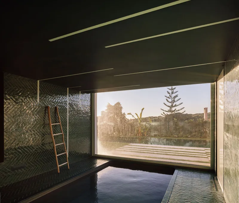 Interior pool room with herringbone green tile walls and large window framing garden view at golden hour