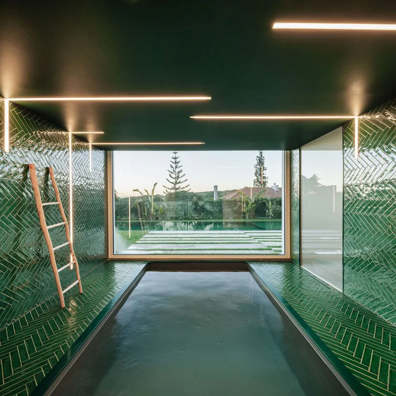 Pool room with recessed linear ceiling lights and panoramic window overlooking hedged garden and trees