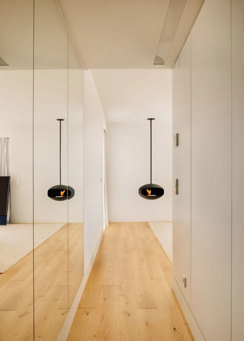 Mirrored corridor with suspended black oval fireplace reflected in floor-to-ceiling mirror panels