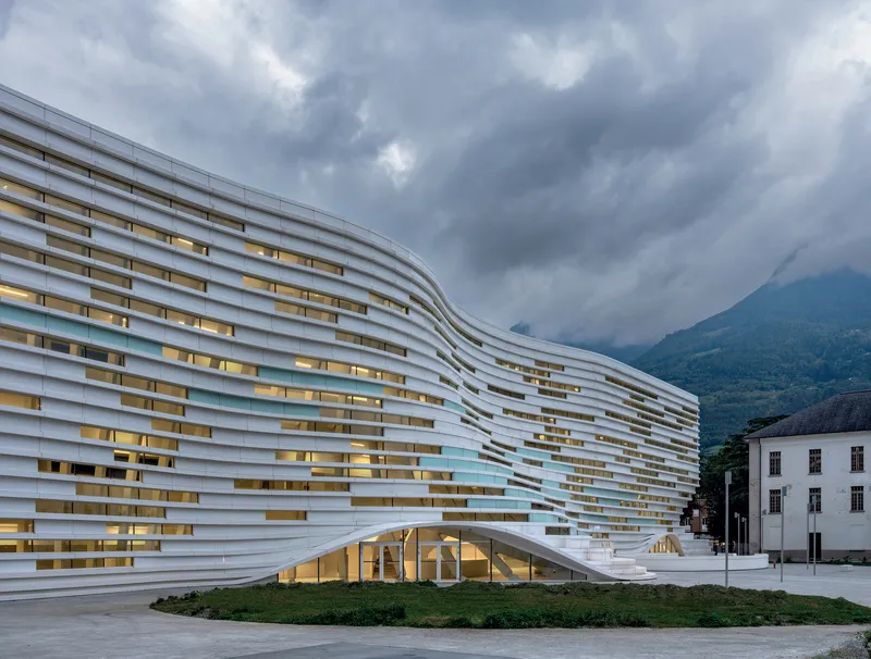 Illuminated horizontal facade at dusk with warm interior lighting visible through staggered window openings