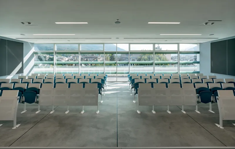 Auditorium with rows of blue chairs facing full-height glazing overlooking a terrace