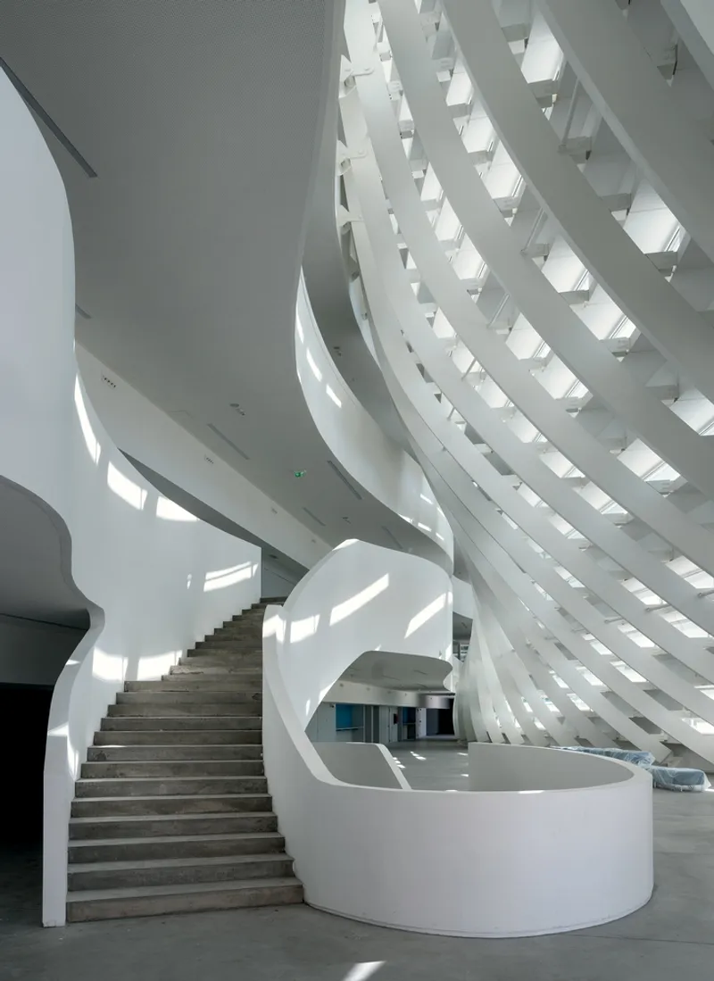 Interior atrium with helical staircase and geometric skylight casting sharp shadows