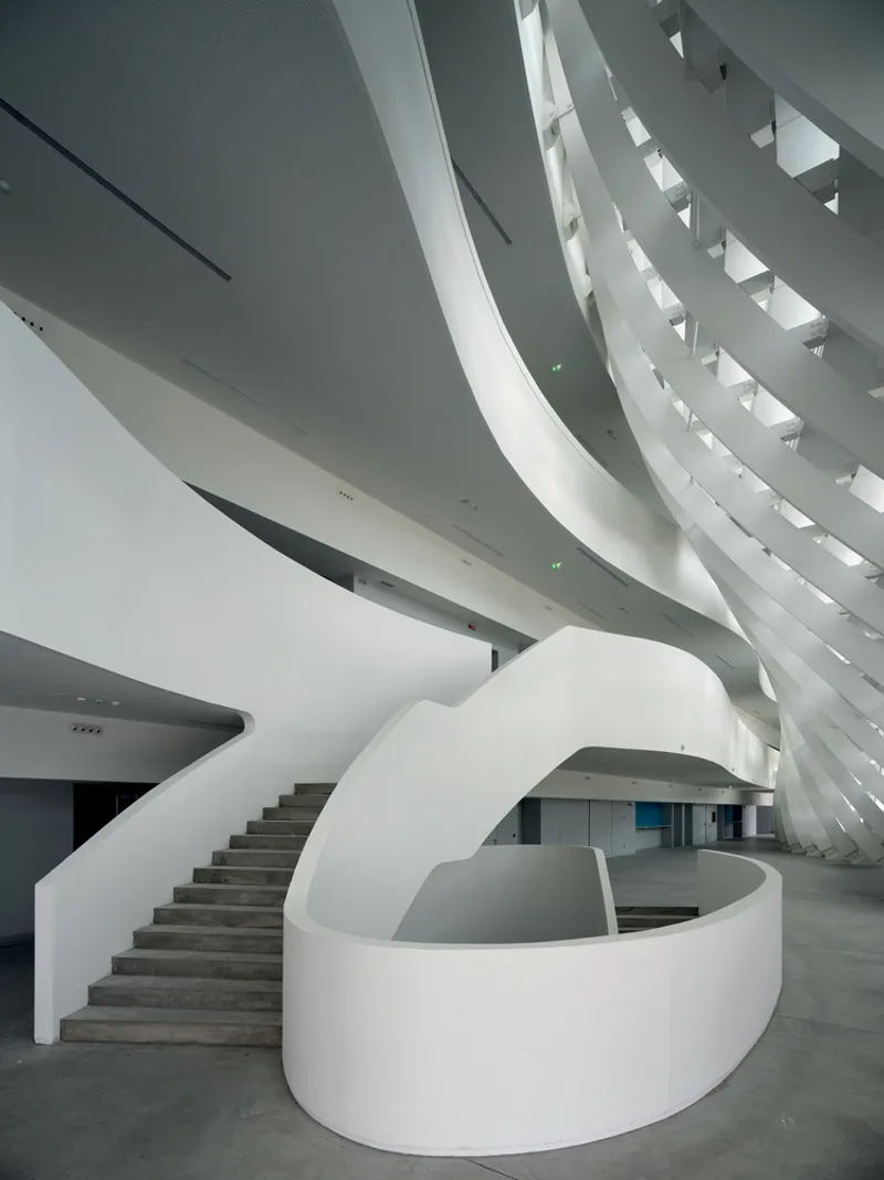 Spiraling staircase beneath angled skylights creating layered shadows in the lobby