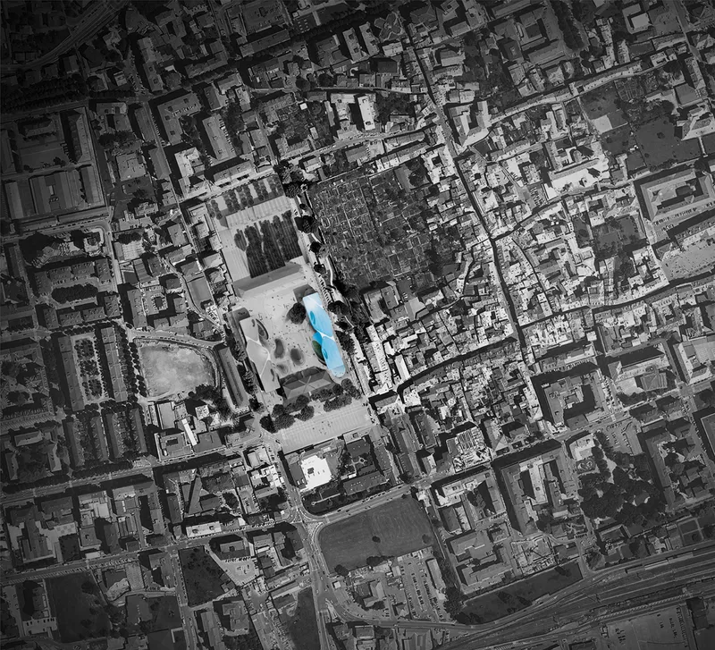 Aerial view showing a blue-tinted building among dense urban blocks in greyscale