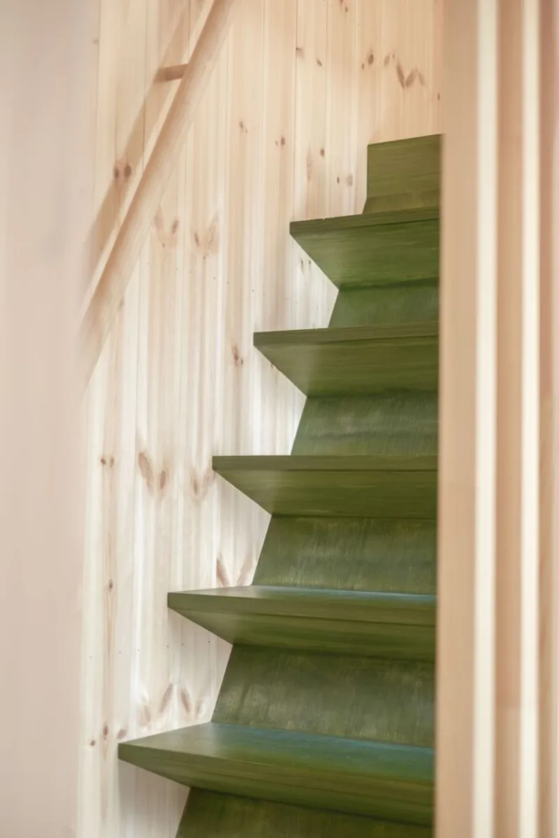 Green-stained timber staircase with cantilevered treads against pale wood paneling