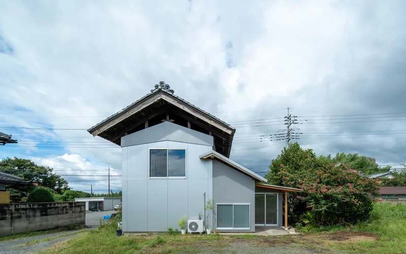 Two-story residence with pale blue cladding and traditional tiled roof under a cloudy sky