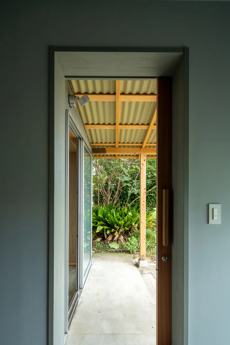 Doorway framing a view through a covered porch with corrugated metal ceiling to planted garden beyond