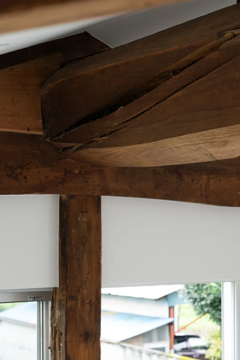 Close-up of intersecting reclaimed timber beams and column joint against a white wall