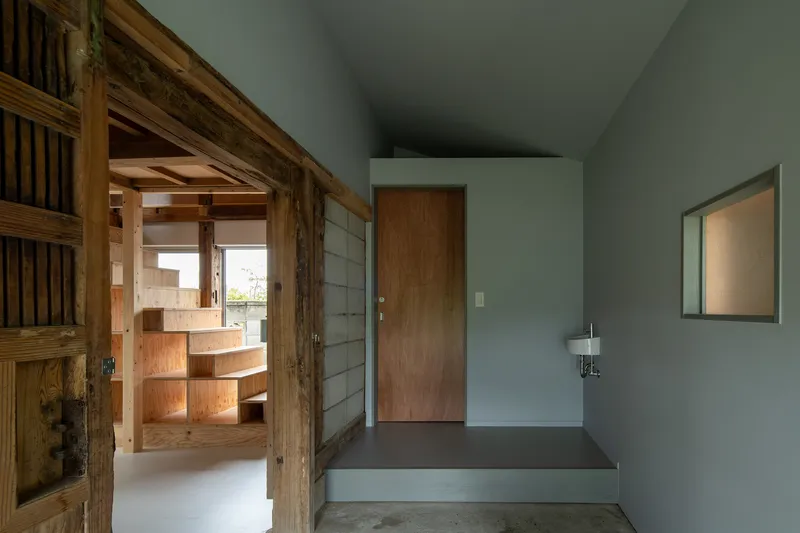 Entry vestibule with sliding timber door opening to view of plywood stairs beyond timber frame