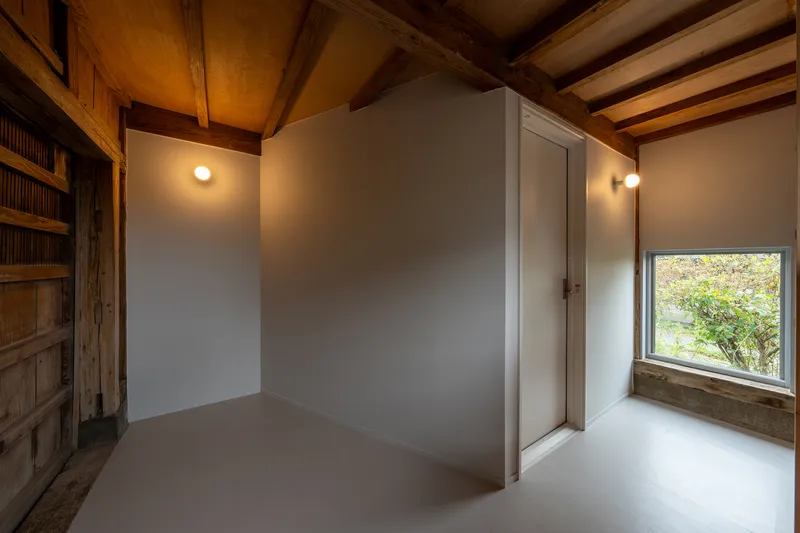 Interior room with white walls and exposed timber beams framing a window overlooking greenery