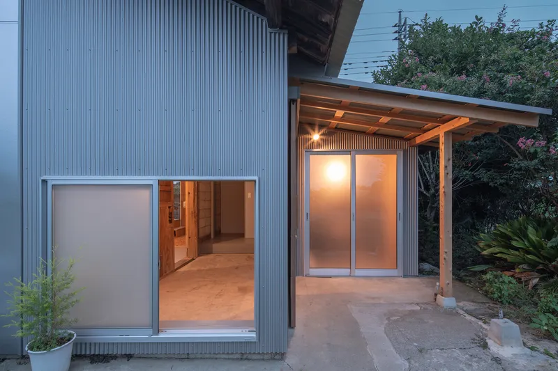 Corrugated metal facade with sliding glass doors opening to interior spaces at dusk