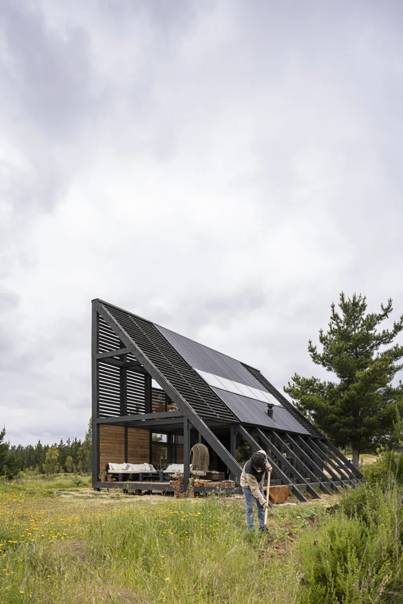 A-frame cabin with louvered black cladding and timber walls in a wildflower meadow with a person nearby