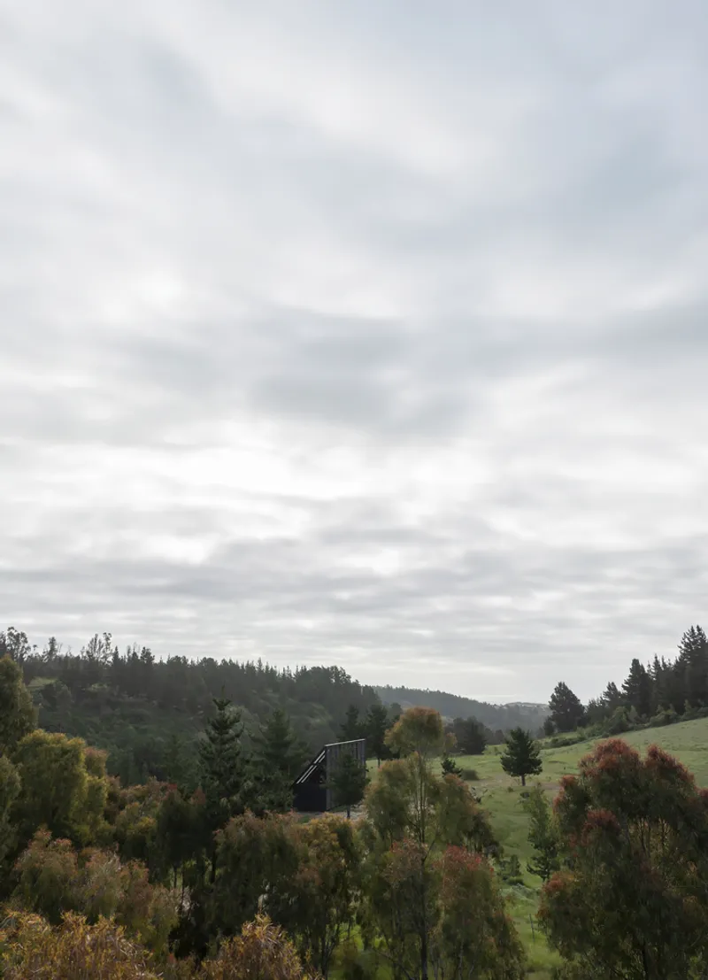 Distant view of the cabin on a hillside surrounded by autumn foliage under a cloudy sky