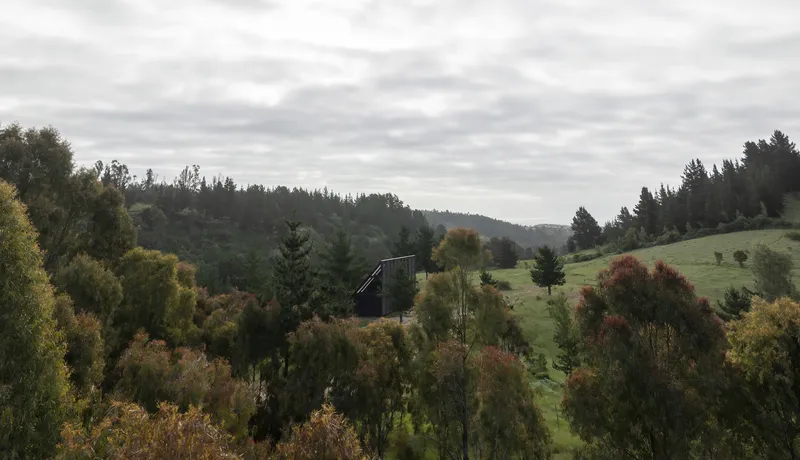 Long view of the dark volume emerging from sloping hillside with autumn foliage and rolling landscape