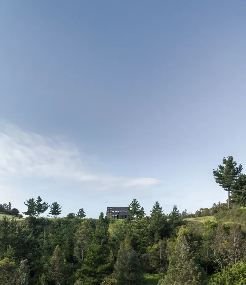 Distant view of the dark box structure perched on a hillside above dense forest vegetation