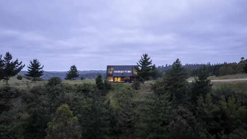 The illuminated interior visible through glazed openings at dusk above forested slope