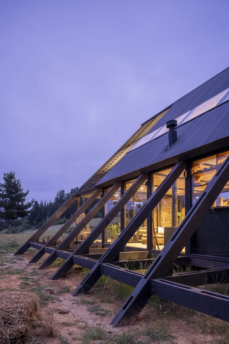 Diagonal steel bracing supporting the sloped glazed facade at twilight with interior lights visible
