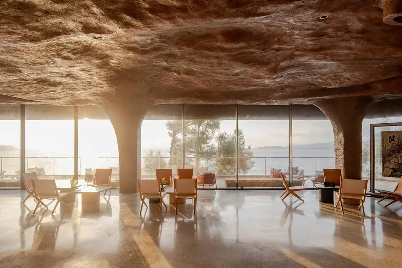 Interior hall with sculpted earthen ceiling and leather folding chairs facing floor-to-ceiling windows
