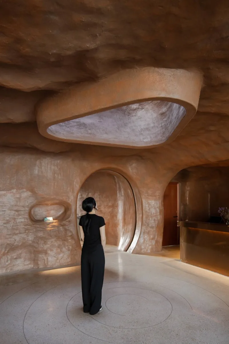 Carved earthen lobby with arched openings and a visitor in black standing beneath sculpted ceiling
