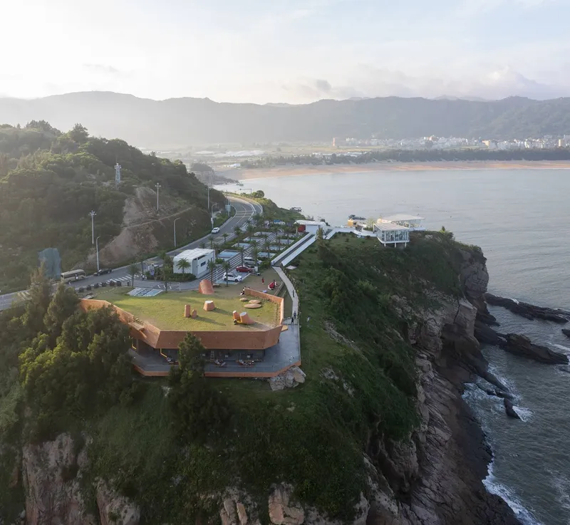 Aerial view of clustered structures on a rocky promontory at dawn with mist over the bay