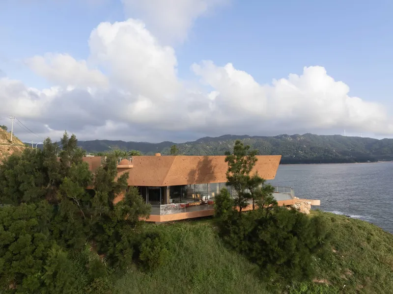 Drone view of the low-profile pavilion with angled roofs nestled among pine trees beside a lake