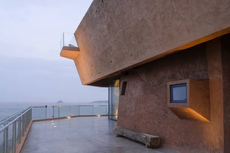 Concrete terrace with recessed window and cantilevered upper volume overlooking the ocean at dusk