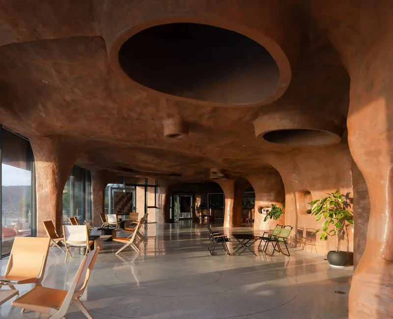Carved terracotta interior with organic ceiling oculi and folding chairs arranged on polished stone floor
