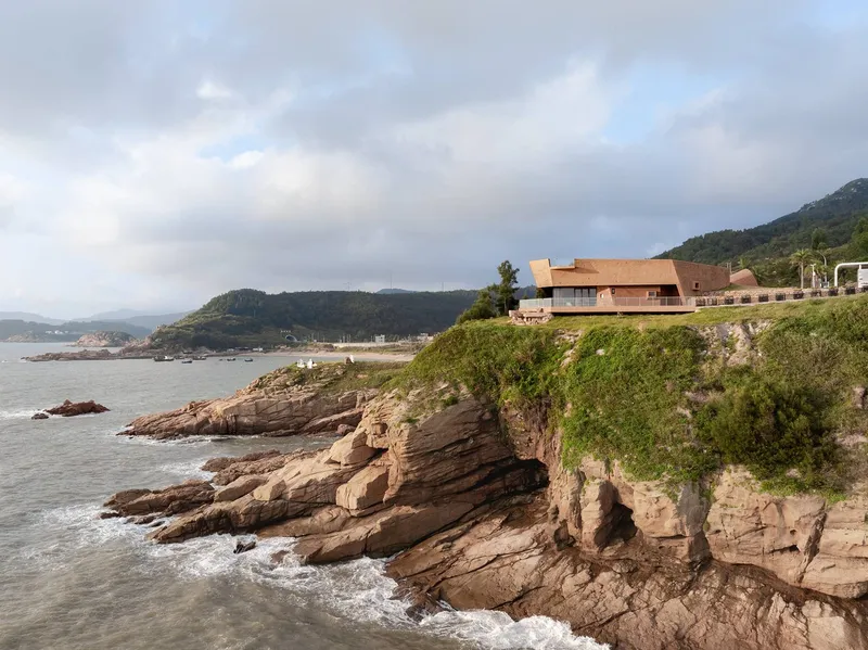Terraced structure perched above layered sedimentary cliffs along the rocky shoreline