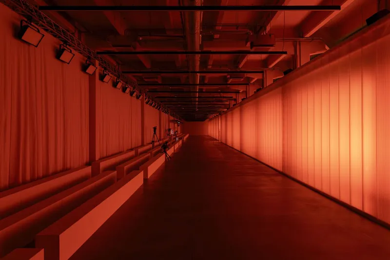 Corridor bathed in red light showing tiered seating and translucent wall panels under exposed infrastructure