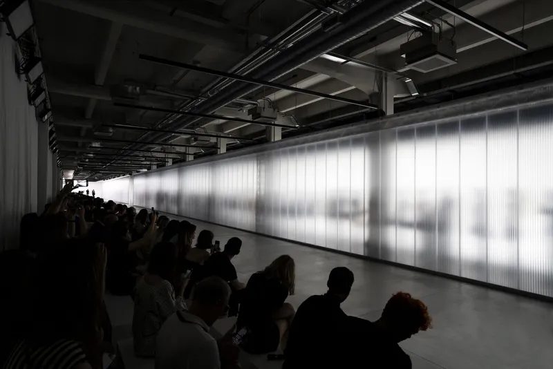 Crowd seated before illuminated translucent wall with silhouettes of figures visible behind the panels