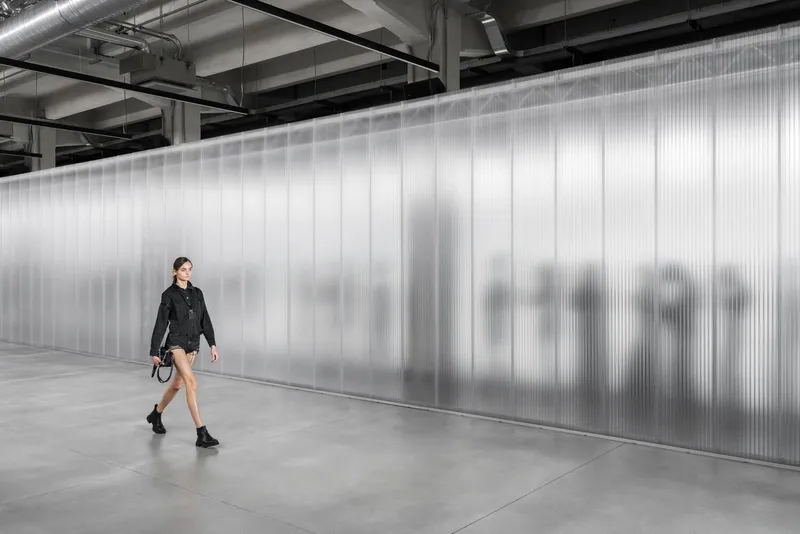 Woman walking past backlit translucent wall panels with silhouettes of people behind them