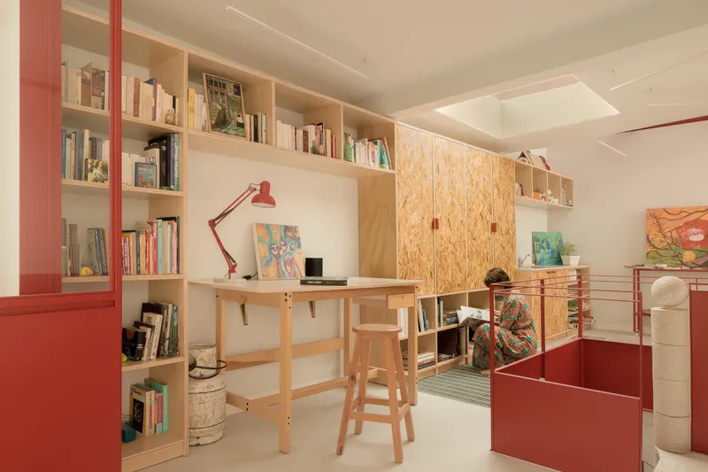 Workspace with plywood desk and shelving alongside red metal dividers under a ceiling skylight